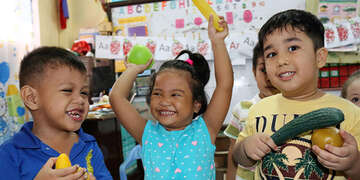 In the Philippines, young children playing with toy produce in classroom.