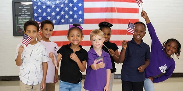 Group of adorable kids holding American flags pose in front of a large American flag