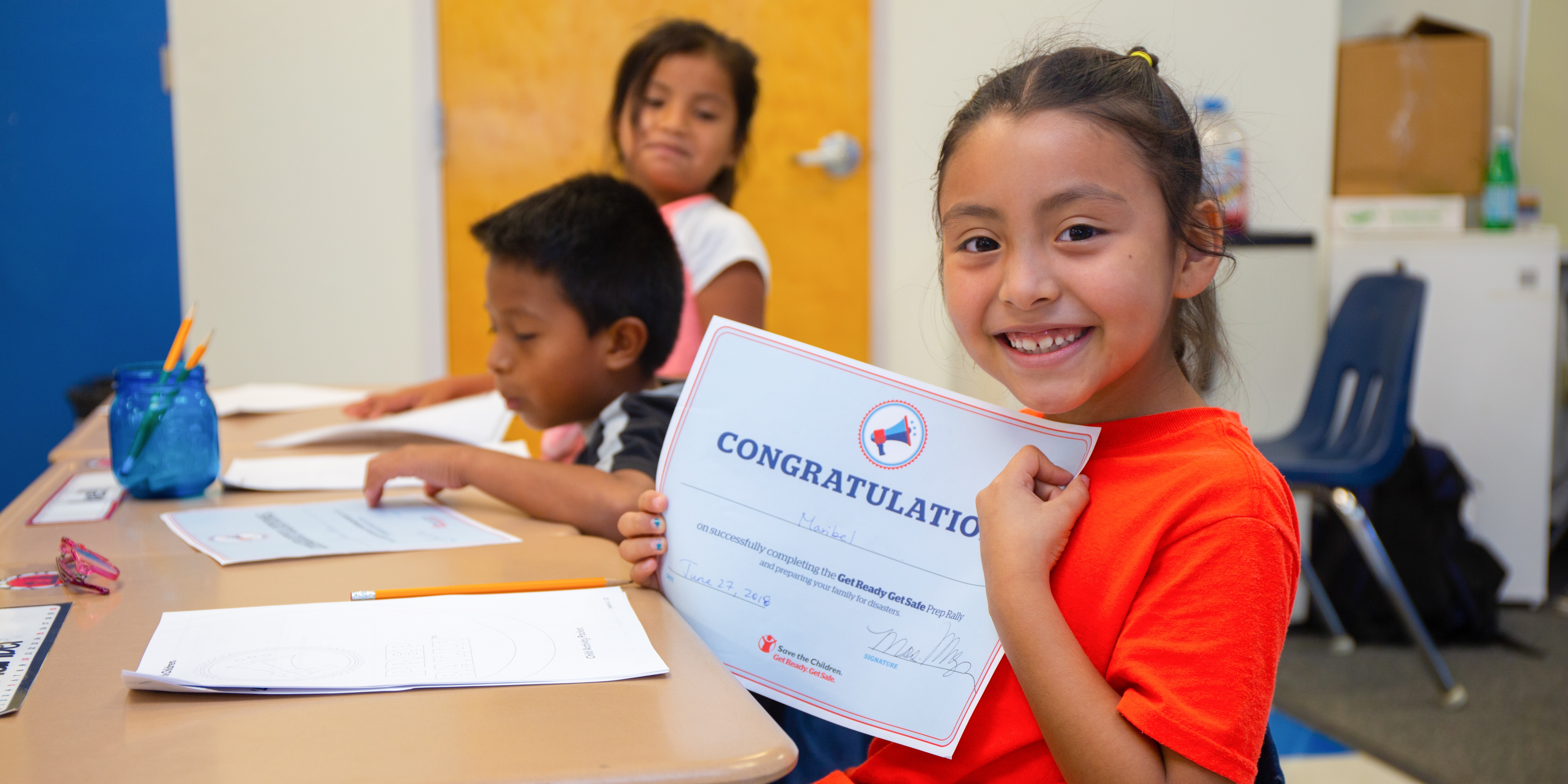 USA, girl in an orange shirt holds up a "congratulations certificate" 