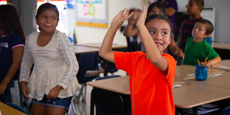 USA, two girls in a classroom dance with their classmates
