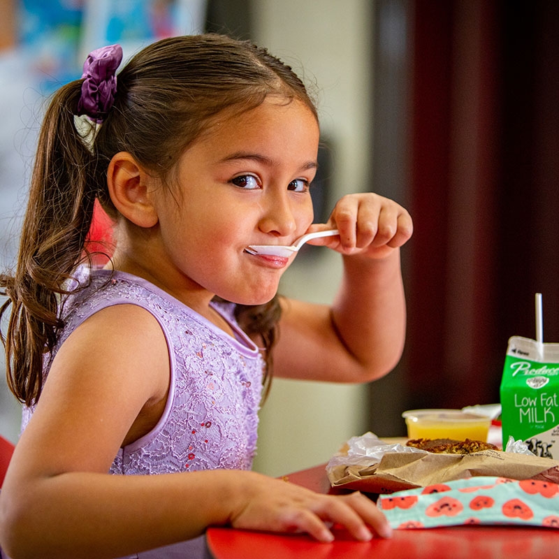 California, USA, a little girl eats breakfast as she looks at the camera