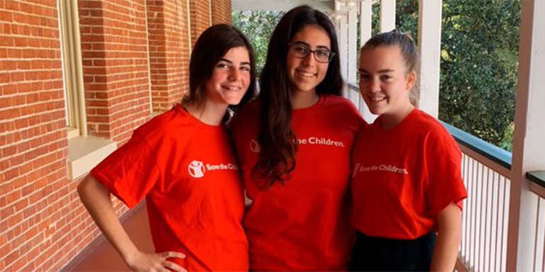 Three high school students stand together in Save the Children t-shirts.