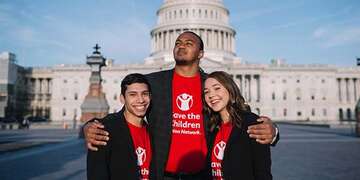 A group of three Student Ambassadors wearing red Save the Children Action Network shirts stand together in front of Capitol Hill during the 2019 Advocacy Summit. 