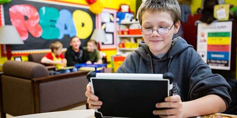 A boy in glasses and a great sweatshirt looking at a tablet.