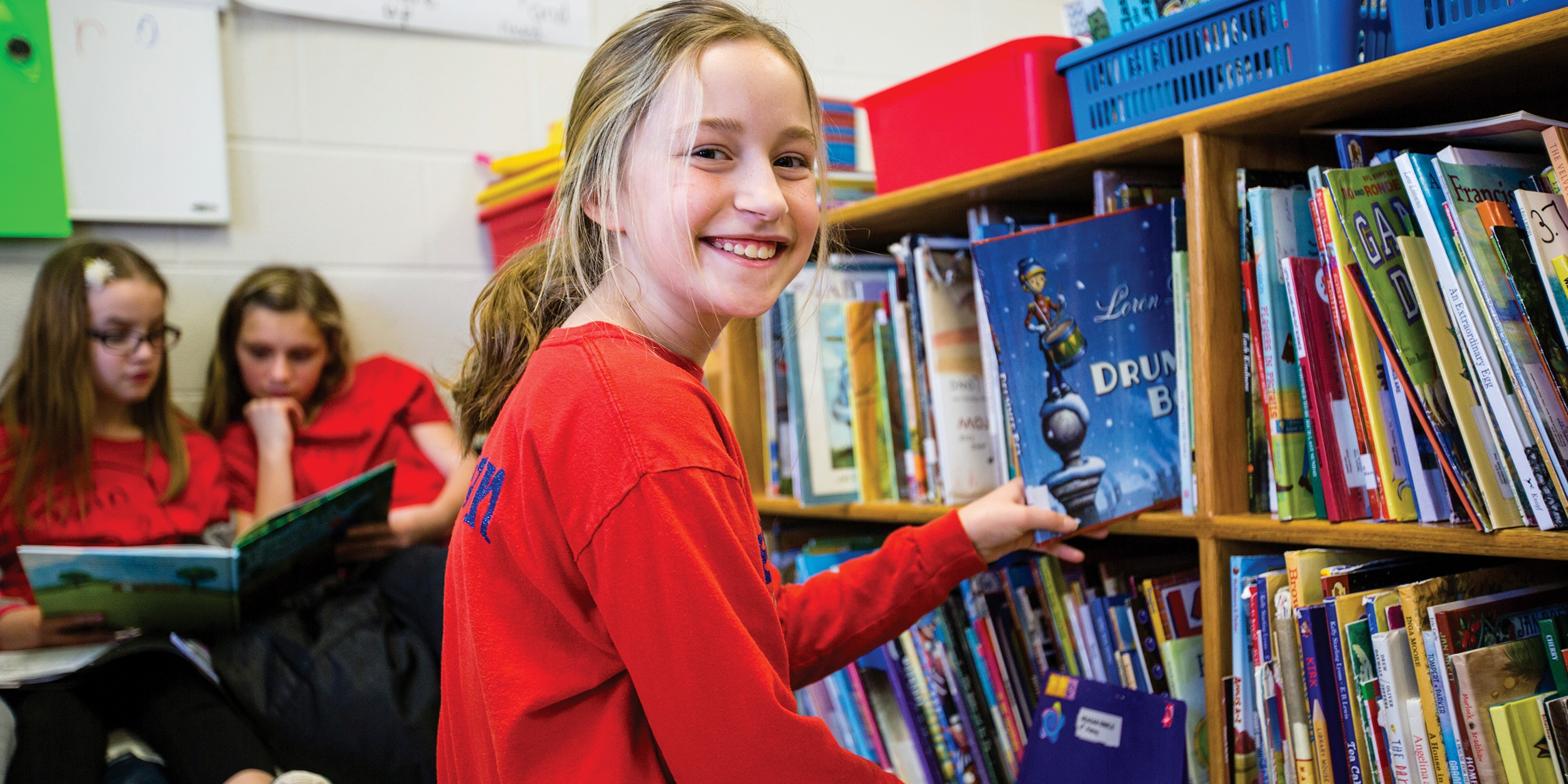 A smiling 10-year-old girl picks a book off a shelf at an in-school literacy program, in Whitley County, Kentucky. Photo credit: Victoria Zegler/Save the Children, December 2017.