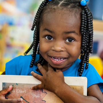 A smiling pre-school student clutches a book to her chest at the Early Steps for School Success program (ESSS) in Barnwell, South Carolina: Photo credit: Susan Warner/Save the Children, October 2014.