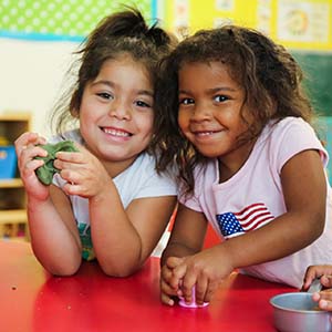 Two girls stand next to each other in a classroom and smile at the camera. 