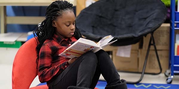 A girl sits in a beanbag chair reading a book.