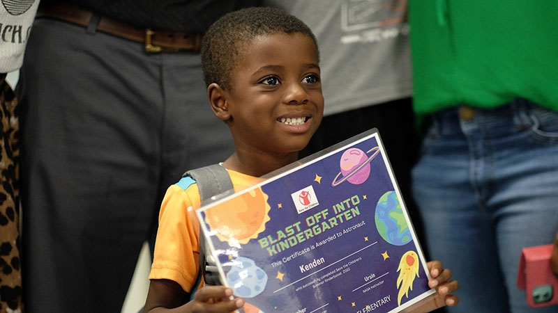 A boy proudly holds his KinderBoost graduation diploma 