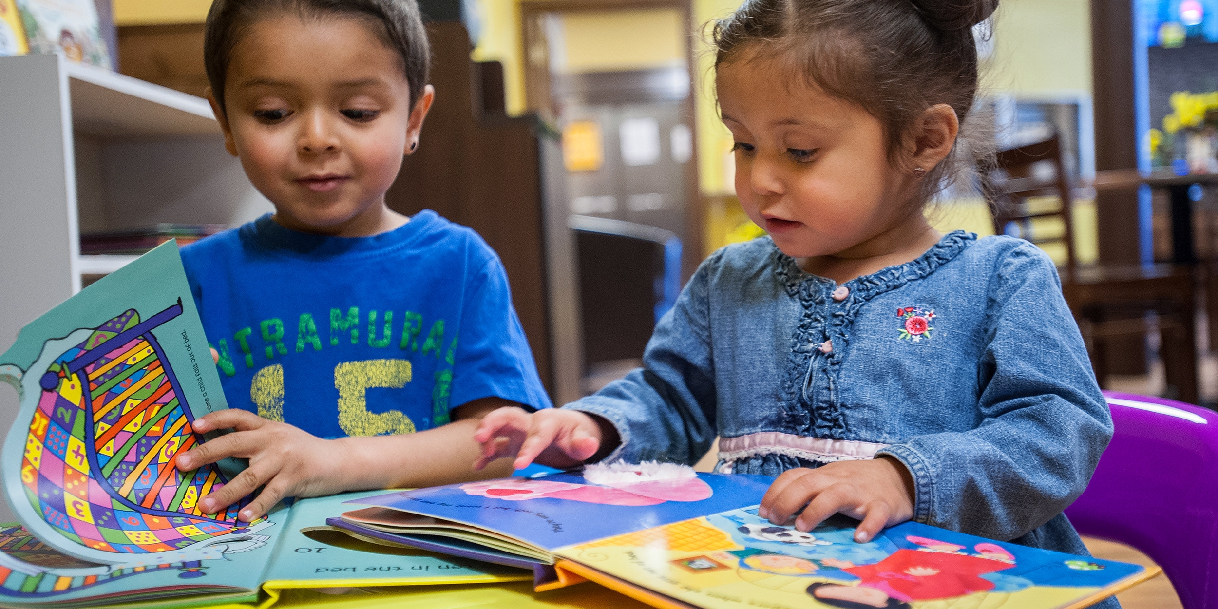 Two young children sit at a table together and look at colorful picture books. Save the Children’s early learning programs promote reading from a young age. Photo credit: Susan Warner / Save the Children, April 2016.