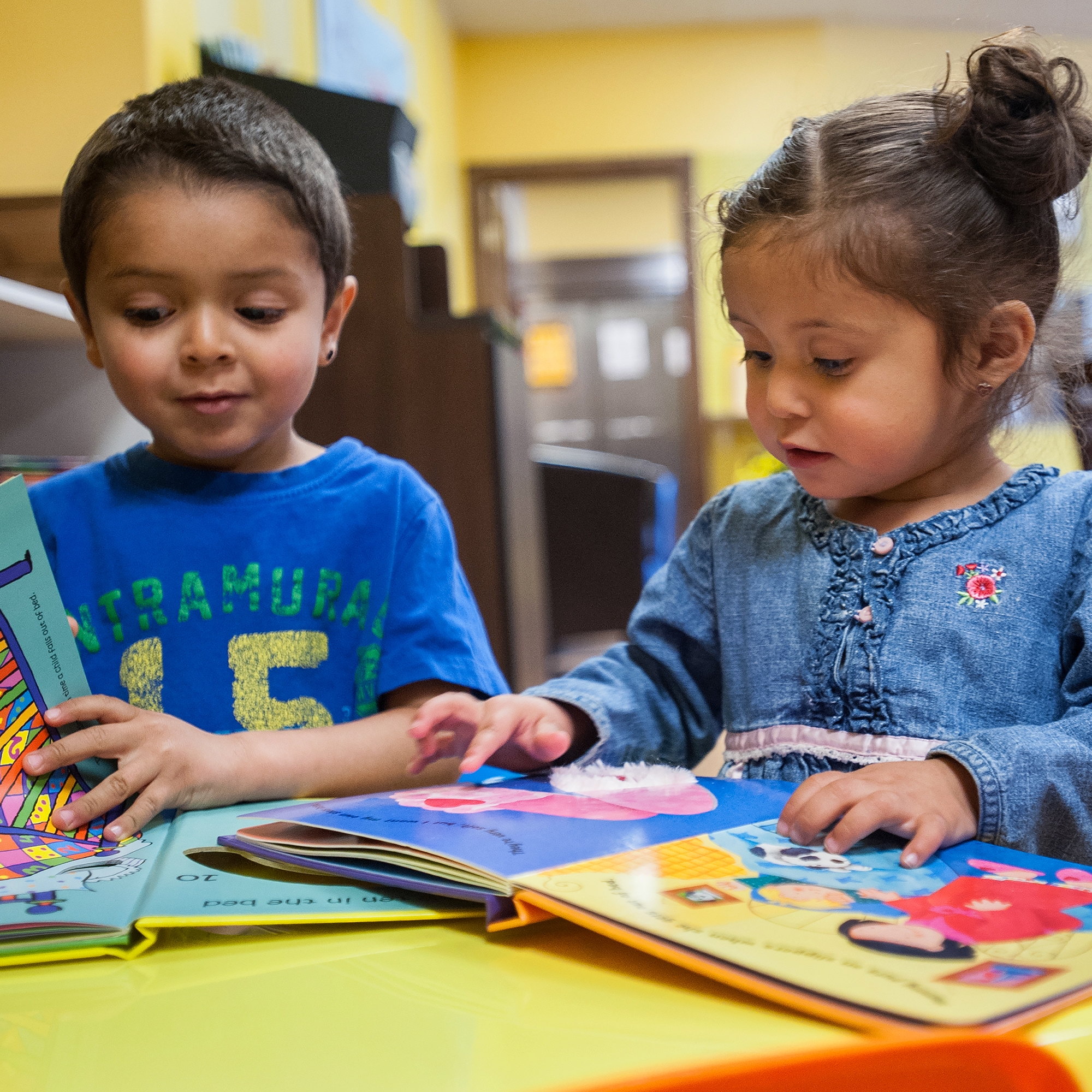 Two young children sit at a table together and look at colorful picture books. Save the Children’s early learning programs promote reading from a young age. Photo credit: Susan Warner / Save the Children 2016.