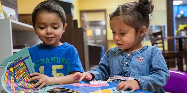 Two pre-k students sit together at a table and read children's books. 