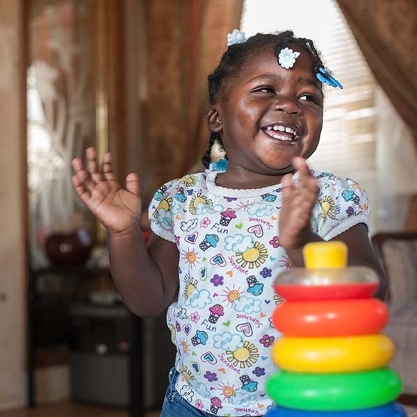 A young girl claps her hands in delight while standing near a set of colorful blocks in her home in Mississippi.