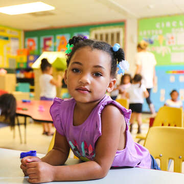 A little girl sitting in a classroom looking at the camera.
