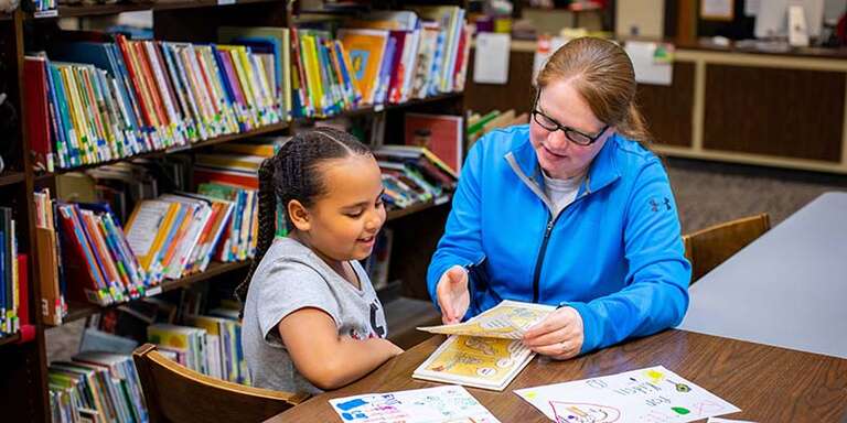 A teacher helping a young girl read.