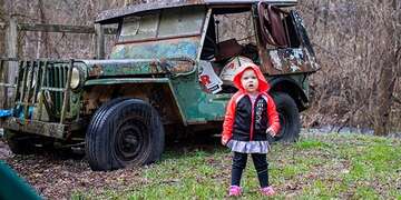 A 2-year old girl stands in front of a rusty tractor in the lawn of her home in West Virgina.