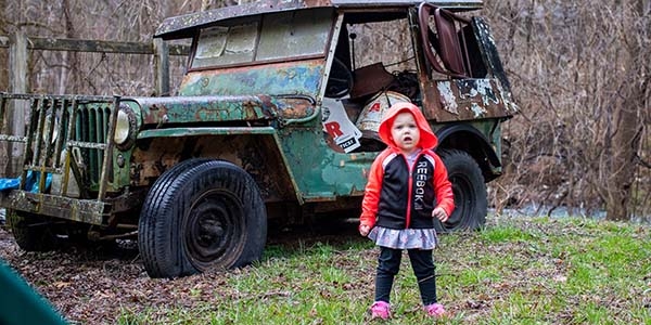 A 2-year old girl stands in front of a rusty tractor in the lawn of her home in West Virgina.