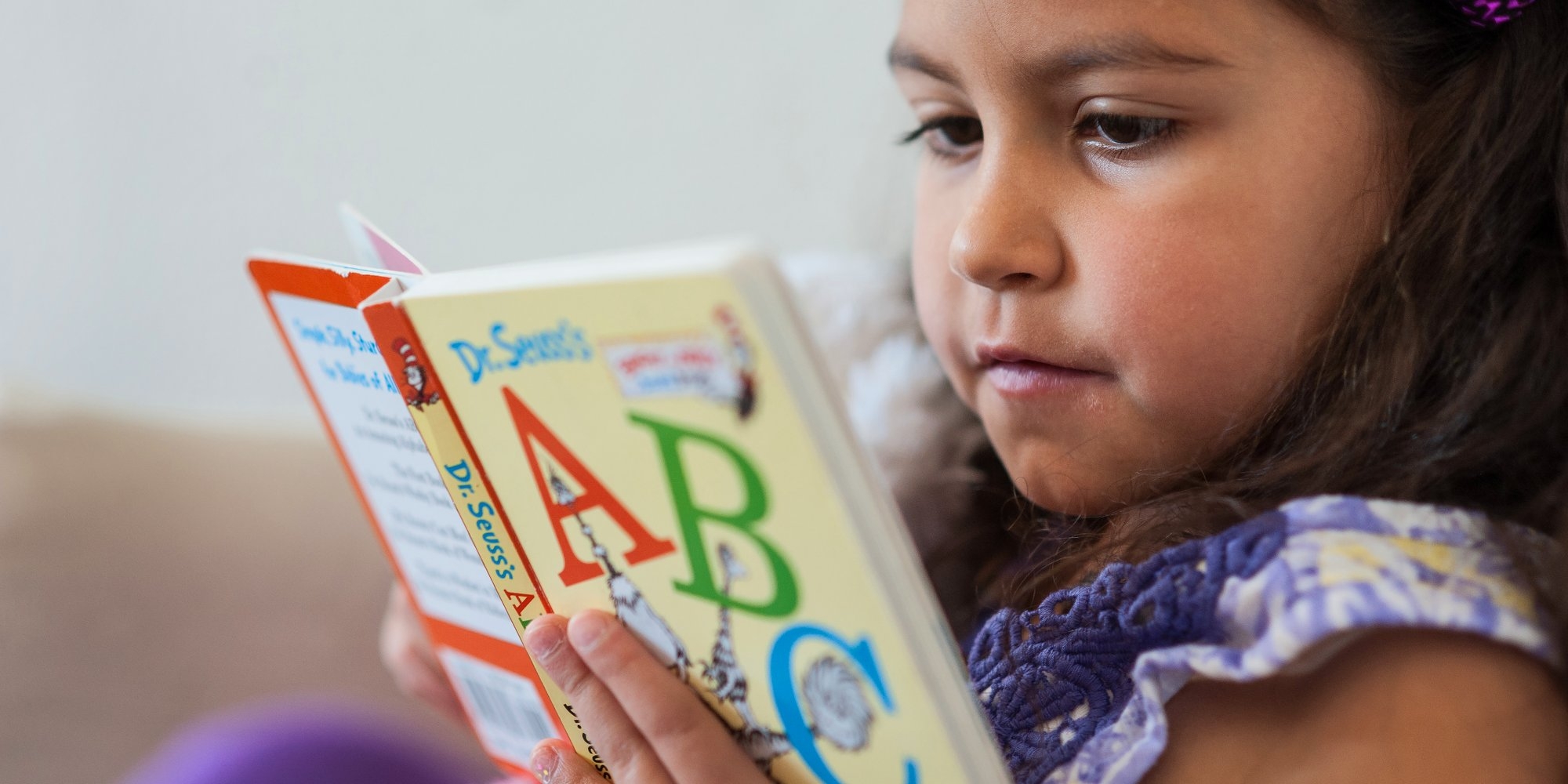 A close up shot of a young girl read a book with ABC on the cover.