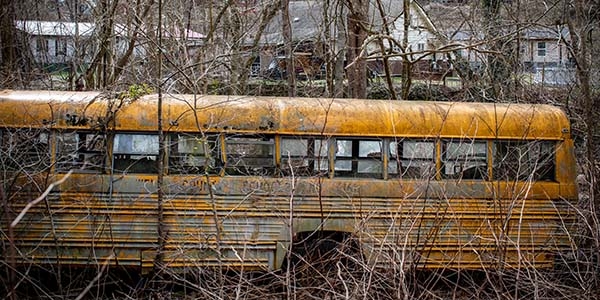 An abandon yellow school bus with broken windows rust in a field in County, West Virginia.