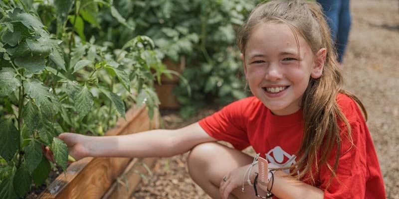 West Virginia, a young girl in a Save the Children red t-shirt, sits in a garden