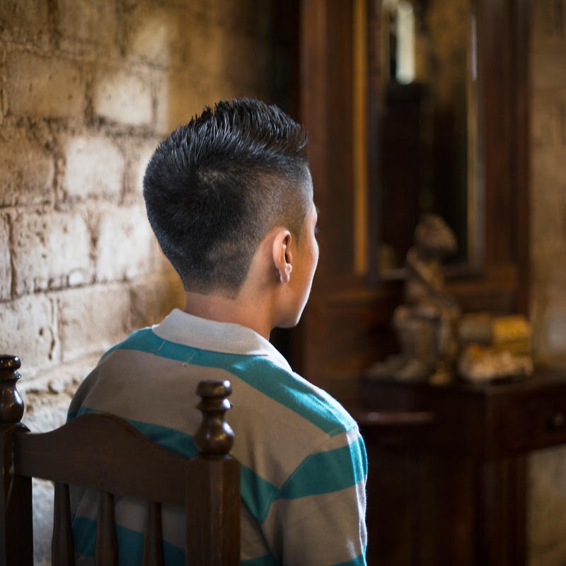 A young boy from El Salvador looks towards a window, his face hidden from view. The boy and his family were forced from their home when a gang threatened their lives.    *Name changed for protection. Photo credit: Tom Pilston/Save the Children, May 2017.