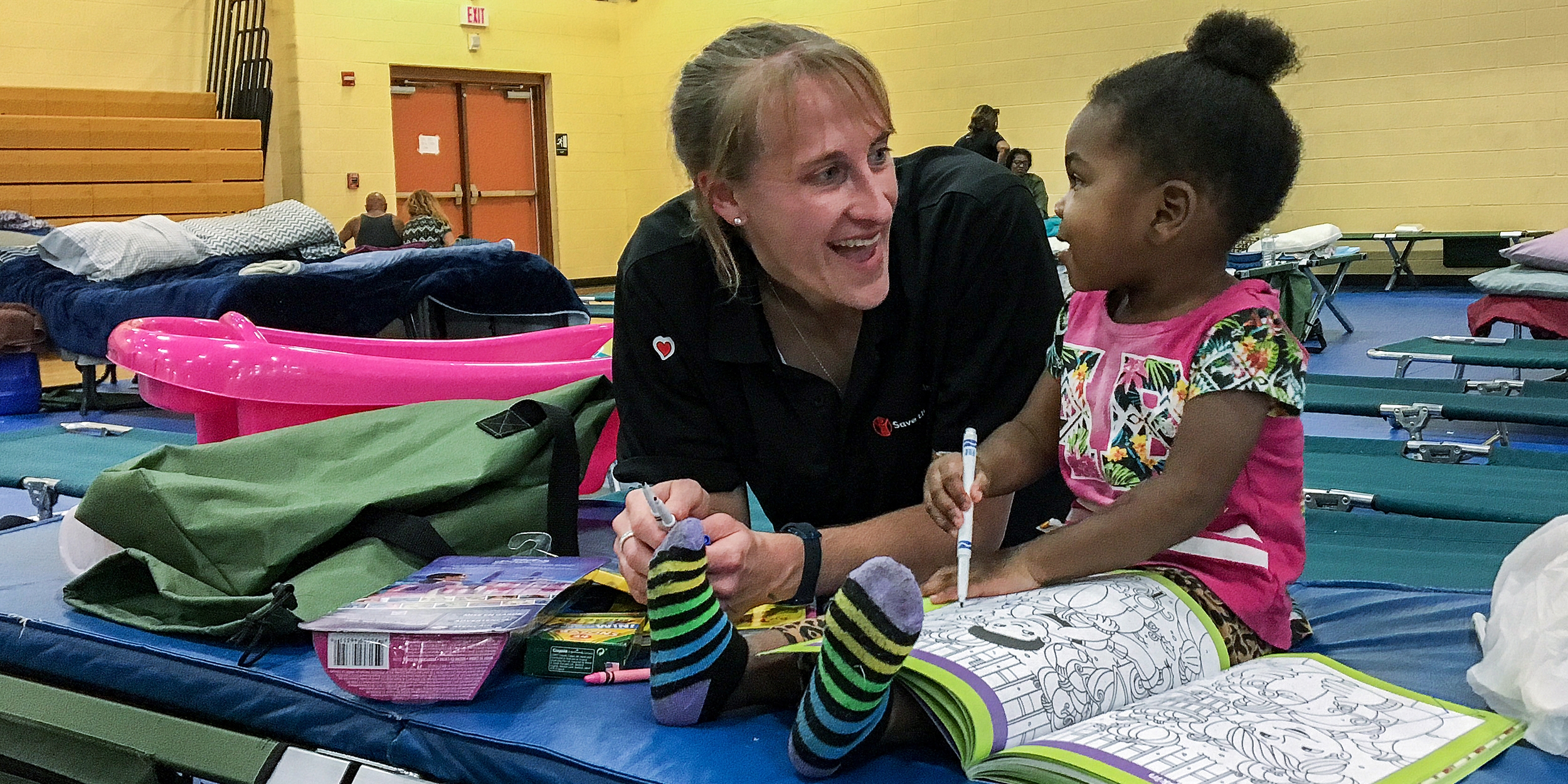 Sarah Thompson, Director of Preparedness for Save the Children, colors with a 2-year-old girl at a shelter in Jacksonville, Florida. Save the Children distributed cribs, infant hygiene supplies and activities to families in the aftermath of Hurricane Irma. Photo credit: Sara Neumann/Save the Children, September 2017.
