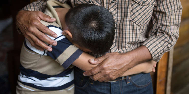 A 12-year old boy buries his face against his father as he mourns the death of his brother in El Salvador. 