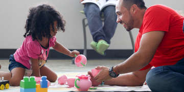 A Save the Children staff member plays with a young child in a child friendly space. 