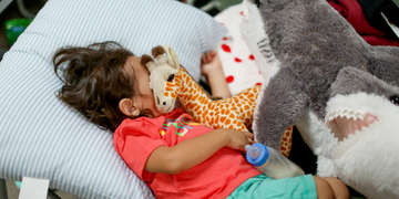 An exhausted one-year-old sleeps soundly, armed wrapped around a stuffed giraffe. The boy is resting at a transit shelter in New Mexico. Today, families who have been released from U.S. Customs and Border Patrol are able to receive food, water and clothing as well as other donated supplies, including children’s stuffed animals, in transit shelters where Save the Children is working. Photo credit: R. Masseo Davis/Save the Children, July 2019.