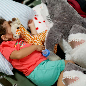 An exhausted one-year-old sleeps soundly, armed wrapped around a stuffed giraffe. The boy is resting at a transit shelter in New Mexico. Today, families who have been released from U.S. Customs and Border Patrol are able to receive food, water and clothing as well as other donated supplies, including children’s stuffed animals, in transit shelters where Save the Children is working. Photo credit: R. Masseo Davis/Save the Children, July 2019.