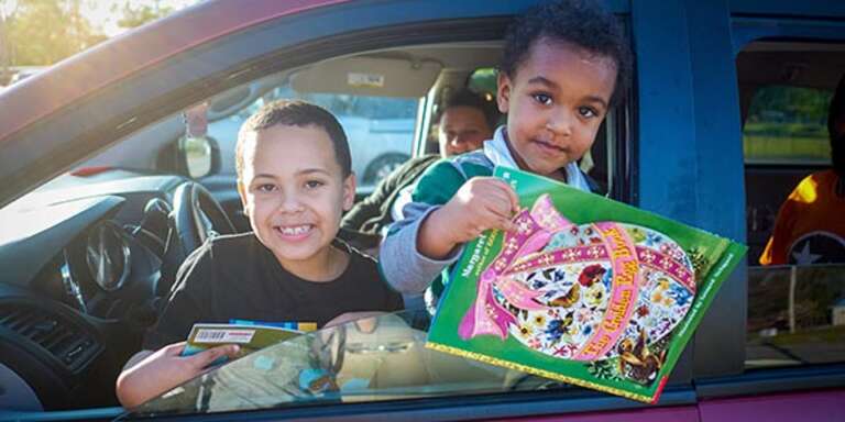 Two boys hold books out of a car window while participating in a social distancing school event in Tennessee. Photo credit: Shawn Millsaps / Save the Children 2020.