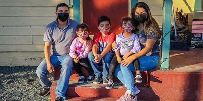 A family of 5 wear face masks to protect against the spread of COVID-19 while sitting outside their home. 