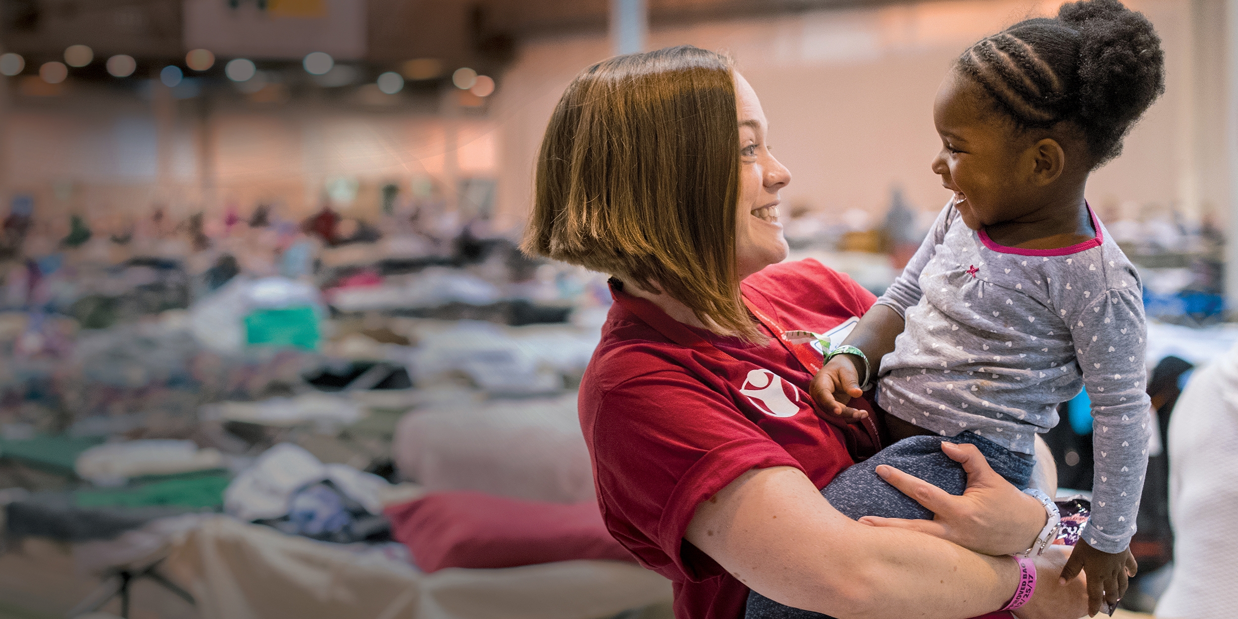 Erin, a Save the Children staff member, smiles at a 2-year old girl in a mega-shelter in Houston. Save the Children distributed cribs and other essentials to families in Texas in the aftermath of Hurricane Harvey. Photo credit: Susan Warner/Save the Children, September 2017.