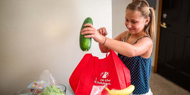 A young girl unpacks a Save the Children meal kit and prepares a garden salad.