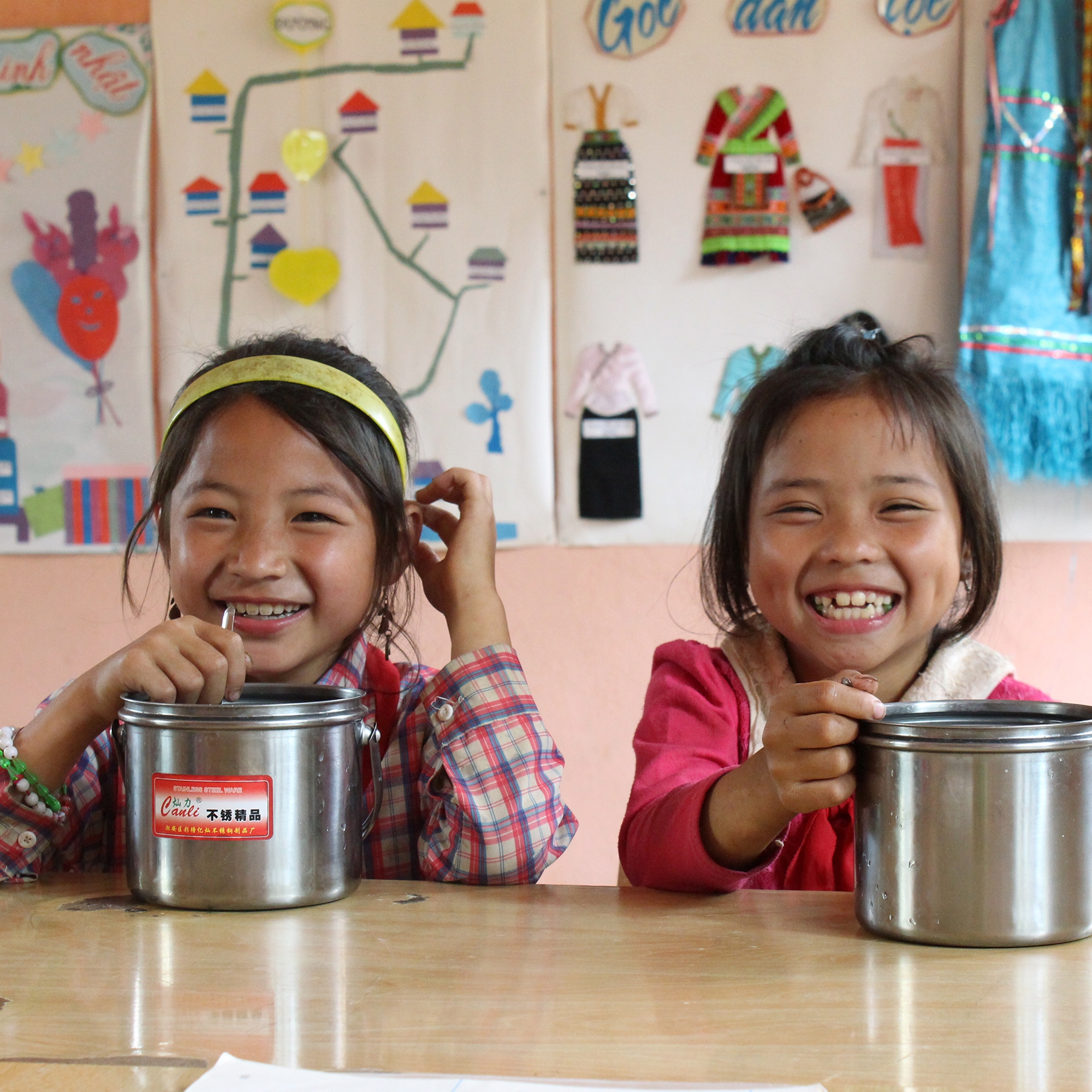 Two smiling schoolgirls in Vietnam eat lunch at a Save the Children-sponsored program. Photo Credit: Save the Children, July 2016. 