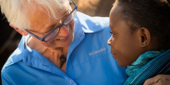 A woman in a blue shirt and glasses smiles at a young girl