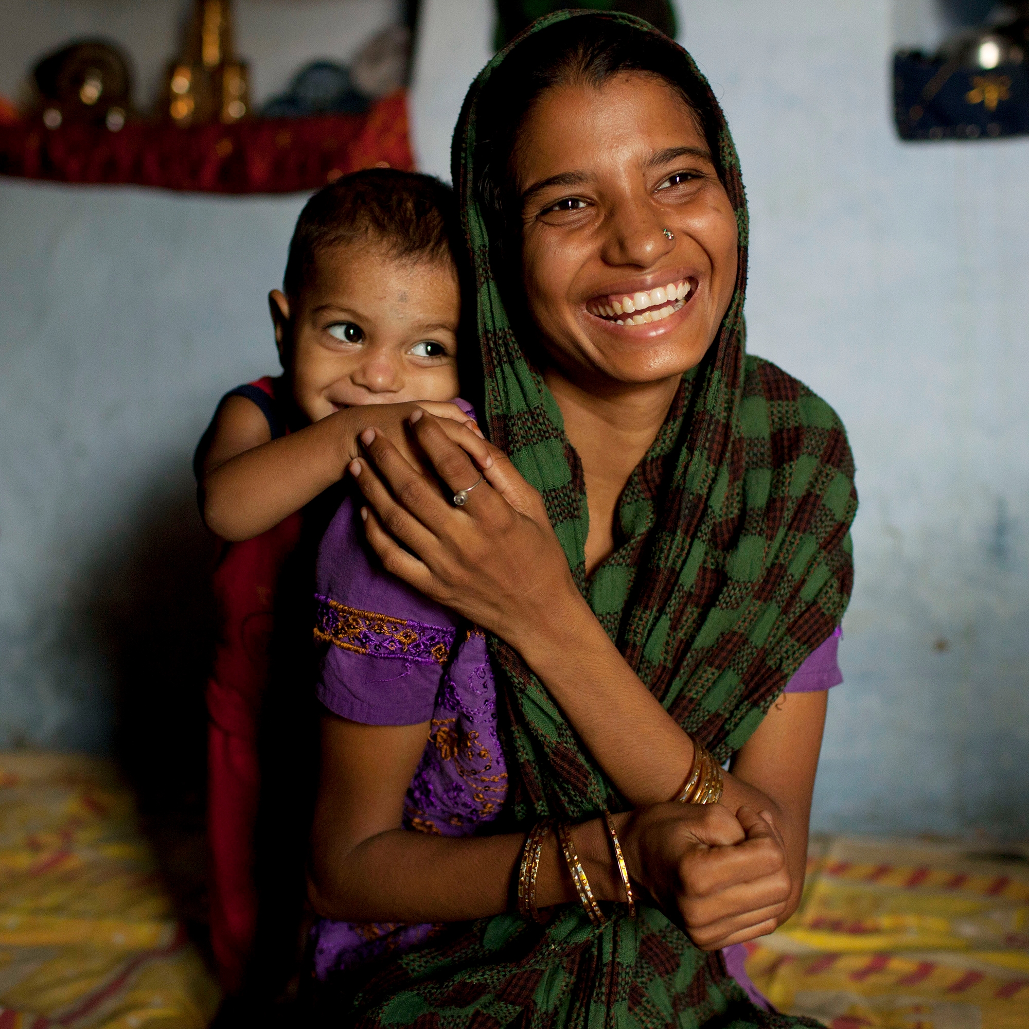 In India, a mother laughs while resting her hand on her young child's arm.